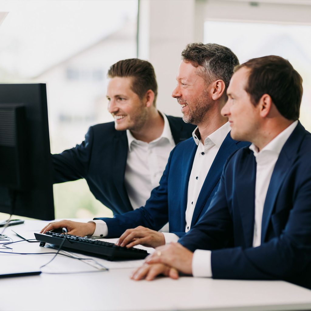 Drei Mitarbeiter der W&L Vermögensverwaltung stehen vor einem Bildschirm und erarbeiten eine Anlagestrategie